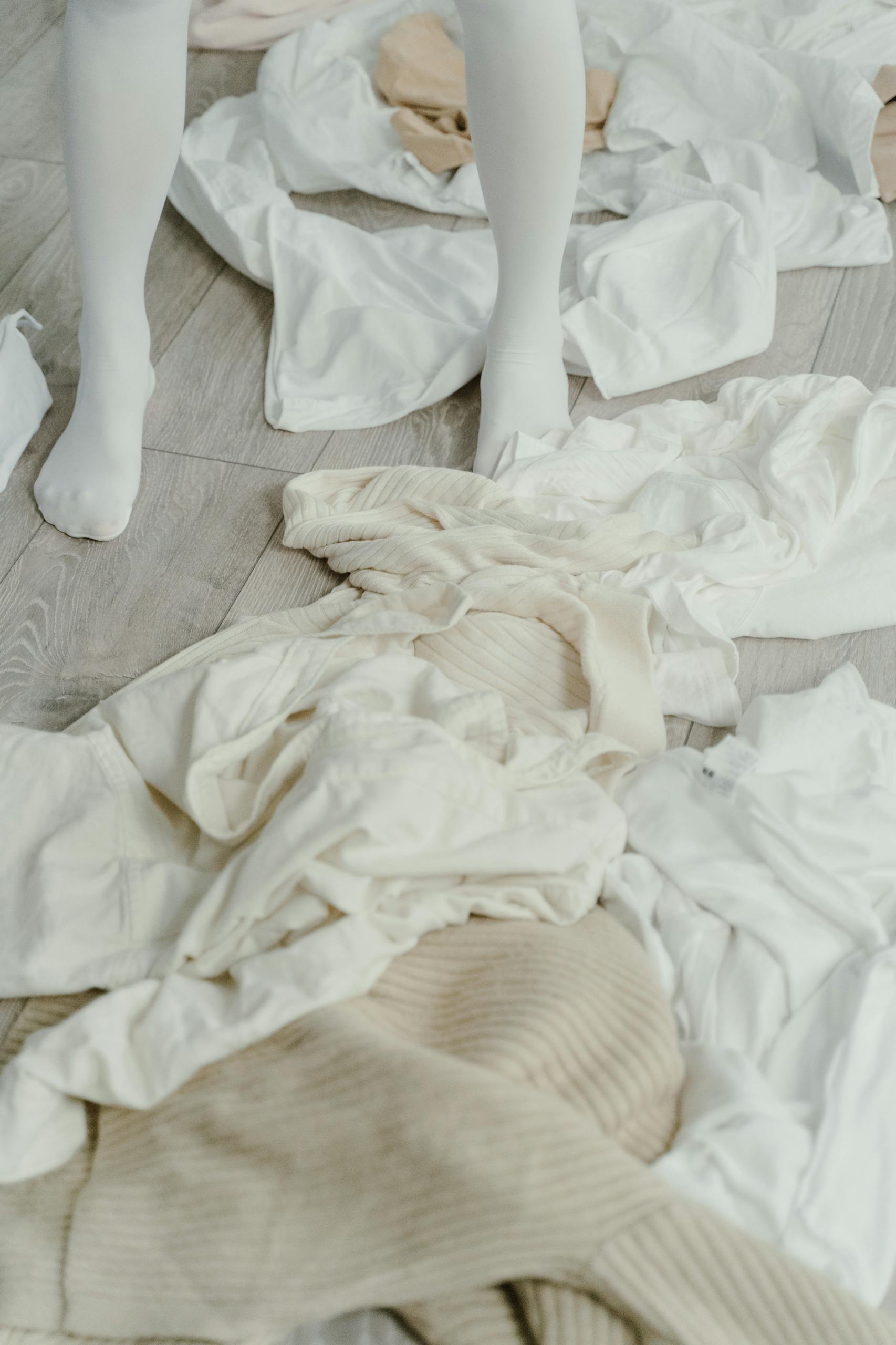 A high angle shot of white clothing crumpled on wooden floor with legs wearing white stockings.