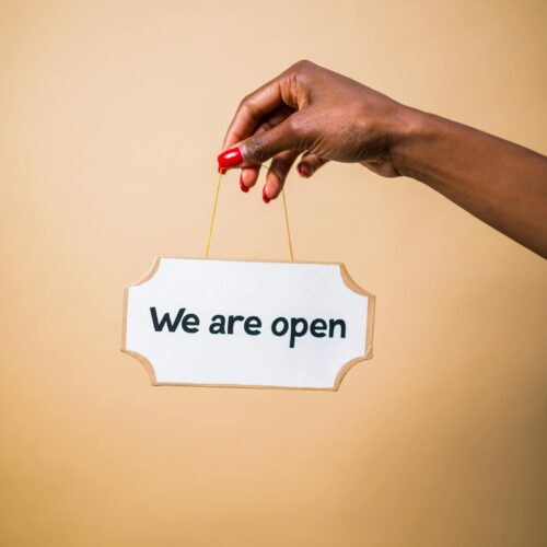 Photo by RDNE Stock project Elegant hand holding 'We are open' sign with a beige background, symbolizing business readiness.